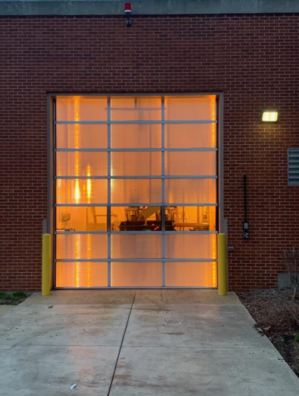 Amber-lit full-view glass overhead door on a commercial building at dusk